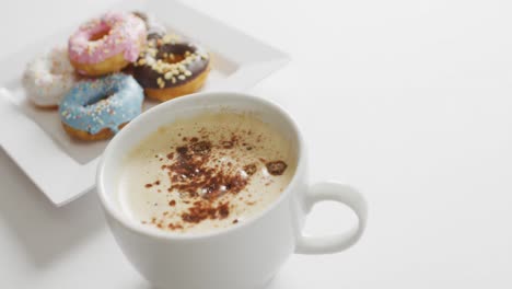 video de rosquillas con glaseado y una taza de café en un plato blanco sobre un fondo blanco