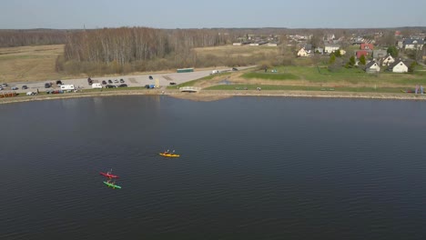 aerial droen footage slowly following 3 kayaks boats who are rowing and paddling on a calm murky muddy brown colored water during a sunny day in southern estonia tamula lake. green shoreline visible.