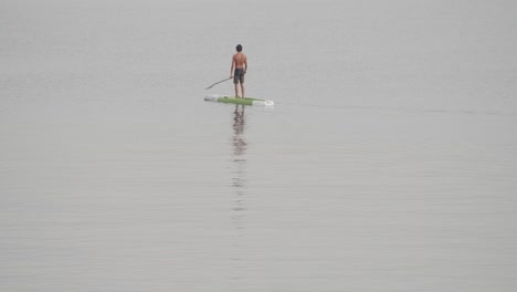 un joven en forma se mueve sin esfuerzo en una tabla de remo en un mar en calma al amanecer en cámara lenta de 60 fps