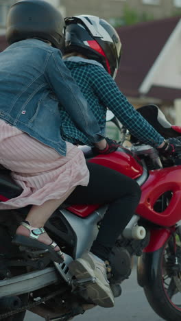 dos mujeres montan una bicicleta eléctrica, con el pasajero sosteniendo al jinete mientras viajan por una carretera urbana, los edificios y los peatones son visibles en el fondo