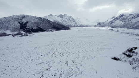 slow aerial dolly pullback of a snow covered valley with mountains shrouded by clouds in the distance, norway