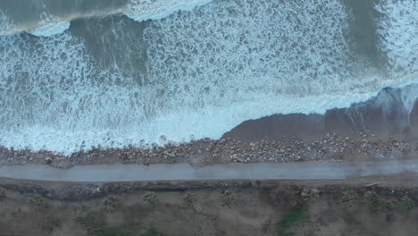 top drone shot captures road leading along the coast line as white foamy waves wash ashore