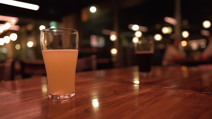 Un bicchiere di birra chiara riposa su un tavolo di legno lucido in un bar poco illuminato