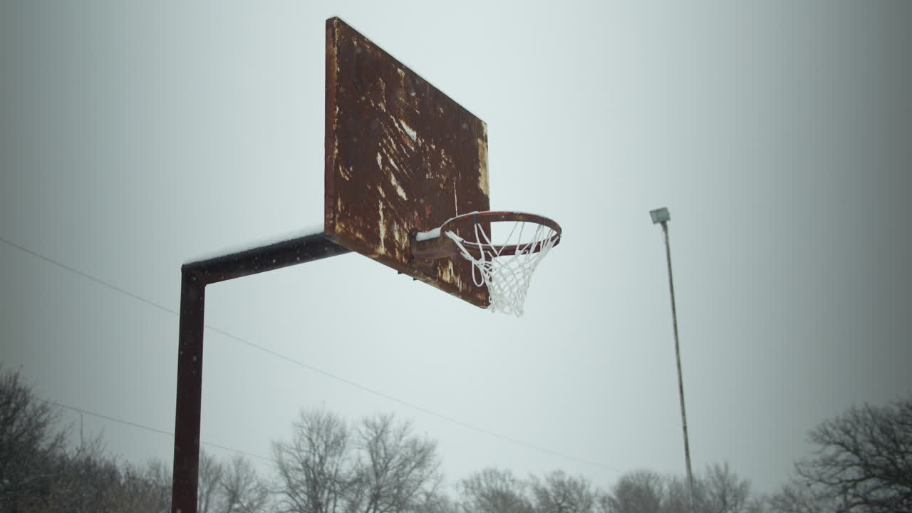 viejo anillo de baloncesto oxidado con copos de nieve en cámara lenta cayendo durante la tormenta de nieve de invierno