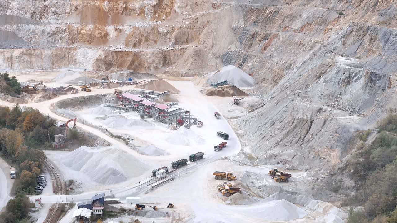 Aerial view of heavy machinery operating at a quarry site, showing industrial excavation, mining equipment, and rugged terrain