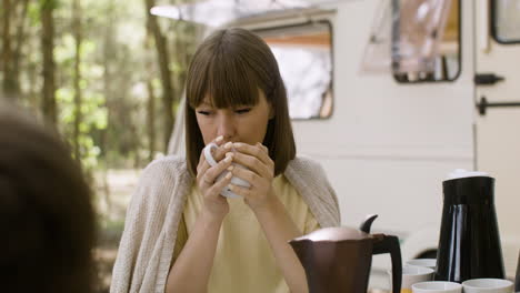 smiling woman drinking coffee while having breakfast with her family at the camping in the forest