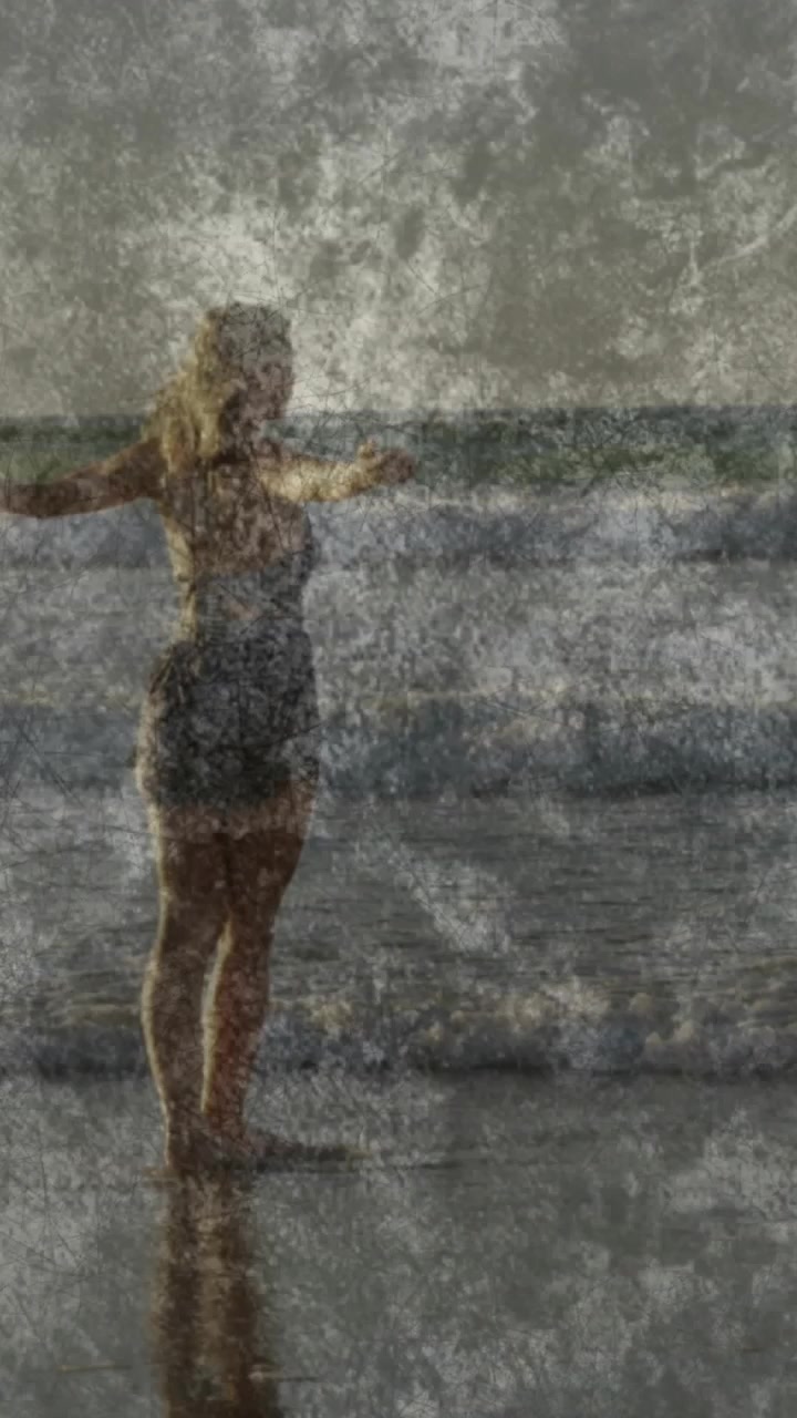 Vertical video: Woman arms open at shore, waves lifting foam overlays and reflecting legs, wellness
