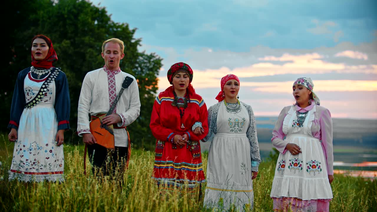 People in traditional folk clothes walking on the field and singing a song - sunset