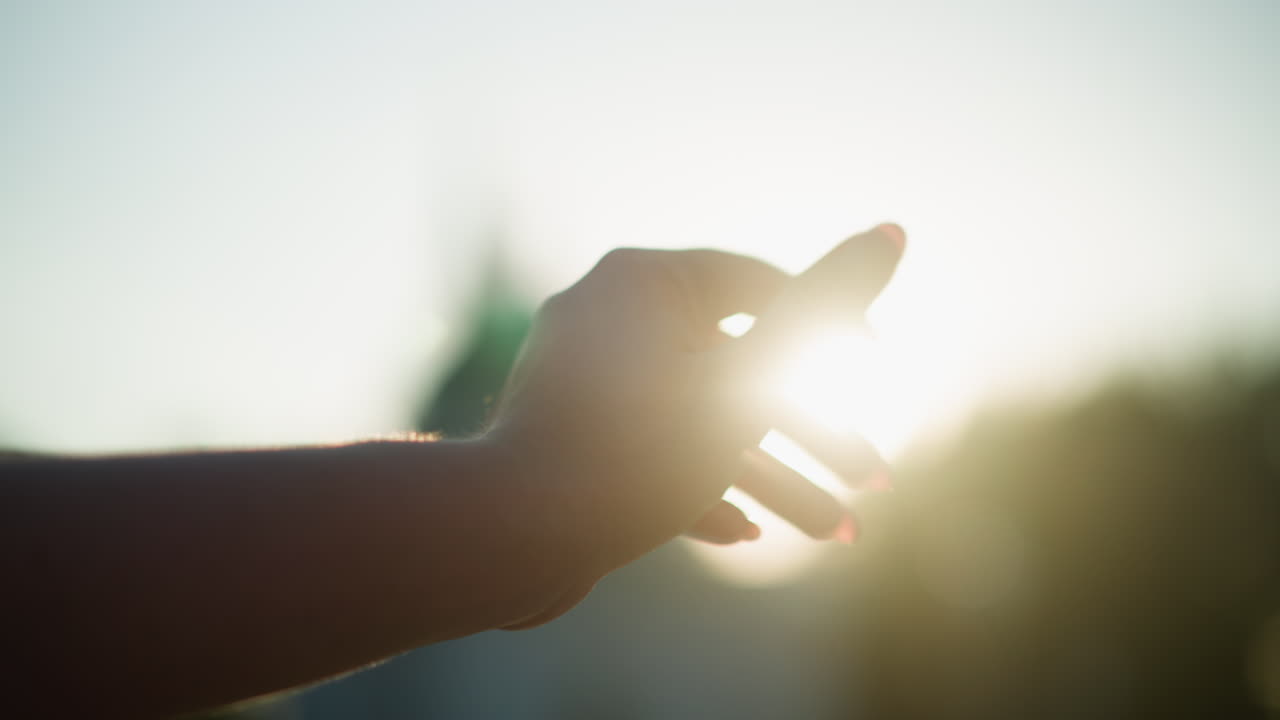밝은 빛을 향해 손을 고, 손가락과 따뜻한 빛 사이의 매혹적인 상호 작용을 만들고, 흐릿한 배경과 함께