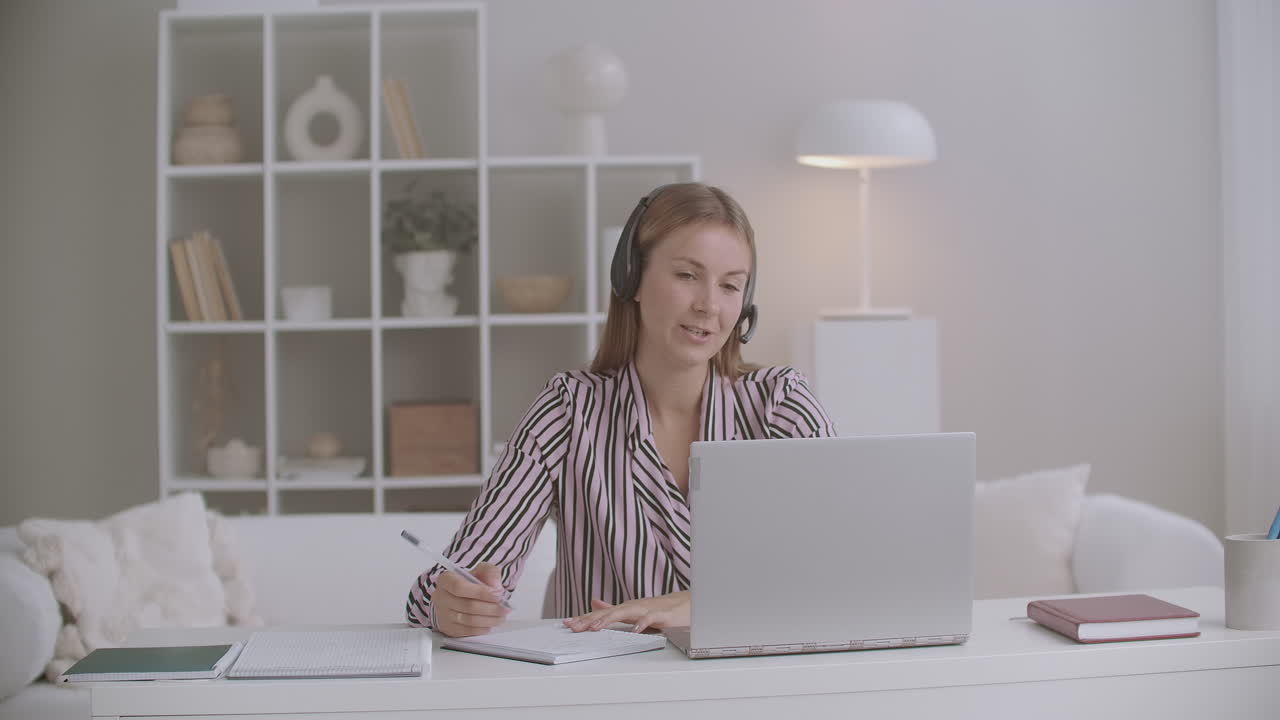 female specialist of call-center or tech support is answering on call of client from home working remotely using laptop