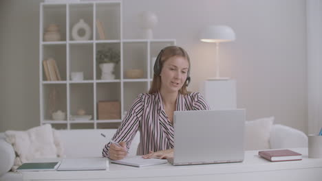 female specialist of call-center or tech support is answering on call of client from home working remotely using laptop