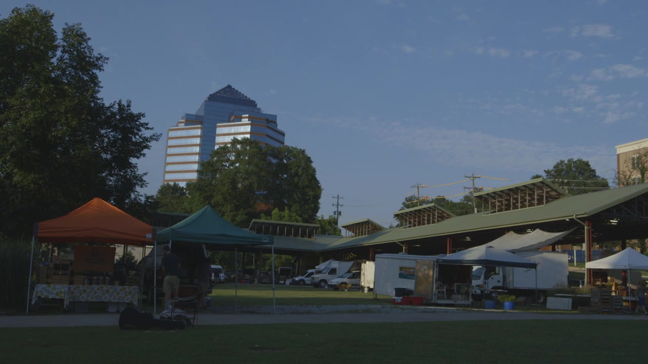 Gente ocupada en el mercado de agricultores de Durham, Carolina del Norte, con el edificio Durham Centre de fondo. Time lapse.