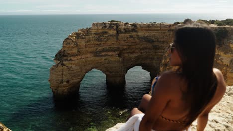 a woman looks out over portugal’s iconic twin sea arches in albufeira, surrounded by turquoise ocean and coastal cliffs