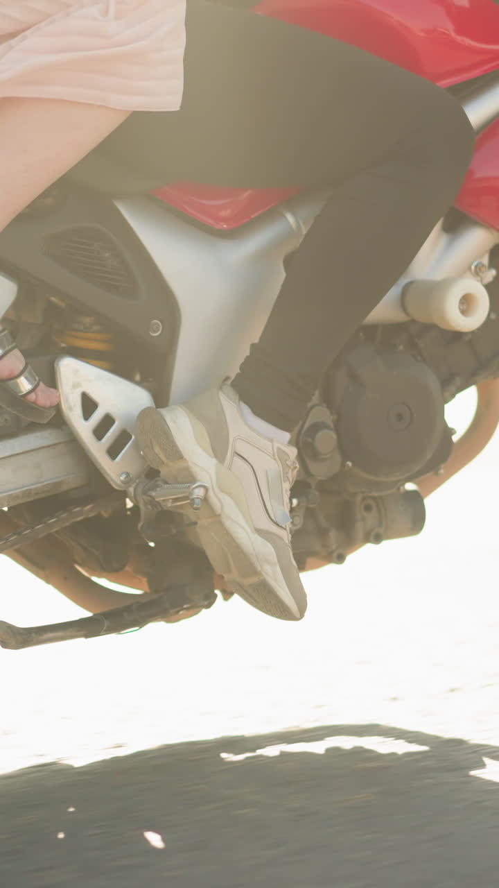 Close-up view of two women riding a power bike in motion, the rider's legs are clad in sneakers, while the passenger wears sandals, with the gown fluttering in the wind as the bike moves