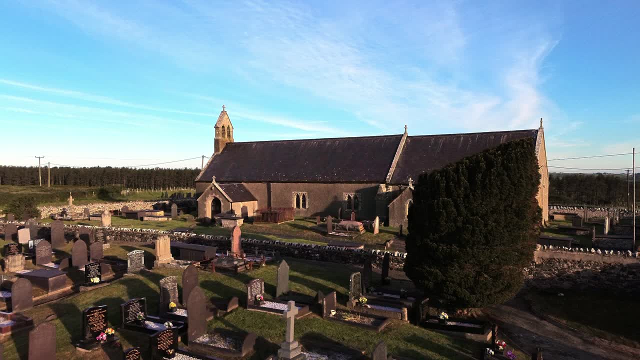 St Peters church in rural Newborough aerial view rising across Welsh slate gravestones at sunrise
