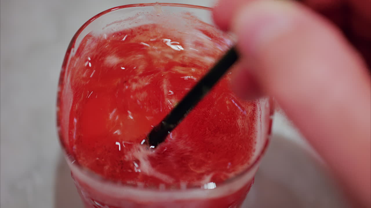 Primo piano di una donna che prepara un cocktail rosso con una cannuccia nera