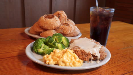 chicken fried steak and sides sit in front of onion rings platter, southern comfort food and soda, slider 4k