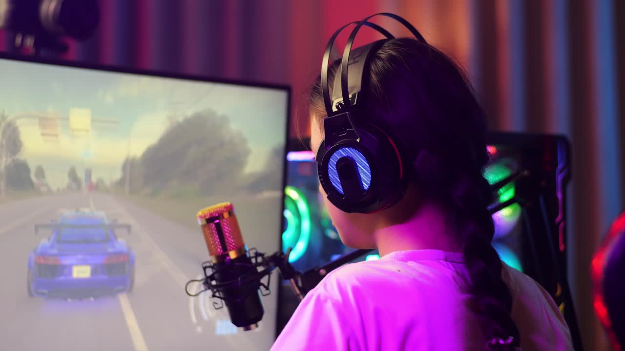 vista de atrás de una chica asiática que juega a un juego de carreras de coches a través de la red en la computadora, hablando por el micrófono. videojuego de transmisión en vivo, escritorio iluminado por luz de tira led rgb