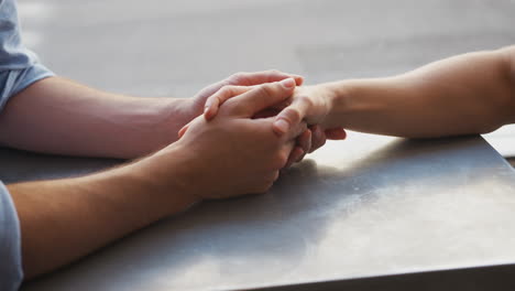 un primer plano de una pareja de hombres homosexuales que se toman de la mano en una cafetería.