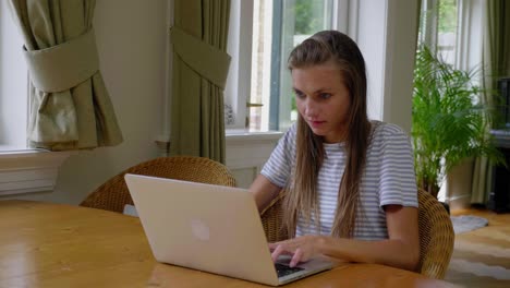 Young-lady-types-on-laptop-on-table-at-home,-pan