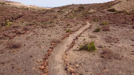 backward aerial dolly over stone-marked path towards acro de tajao