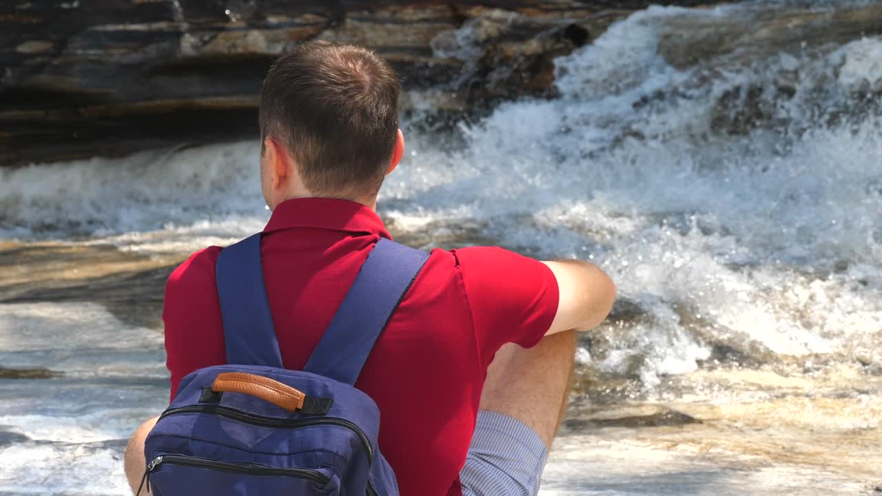 산 강 에 앉아 있는 빨간색 폴로 를 입은 남성 여행자 의 뒷면