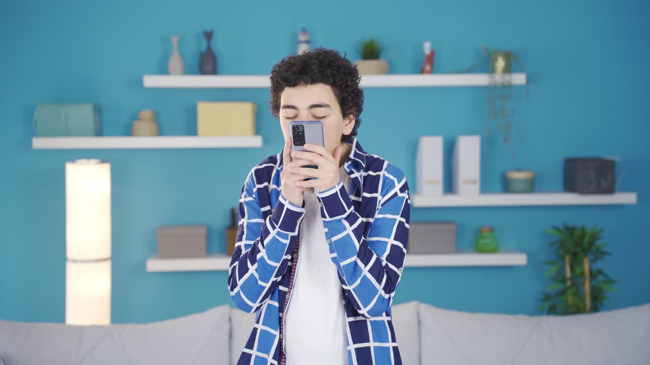 사랑에 빠진 젊은 남자가 행복하게 전화로 문자 메시지를 보내고 있습니다.