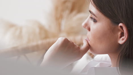 Upset-young-woman-sits-in-armchair-in-light-room-close-view