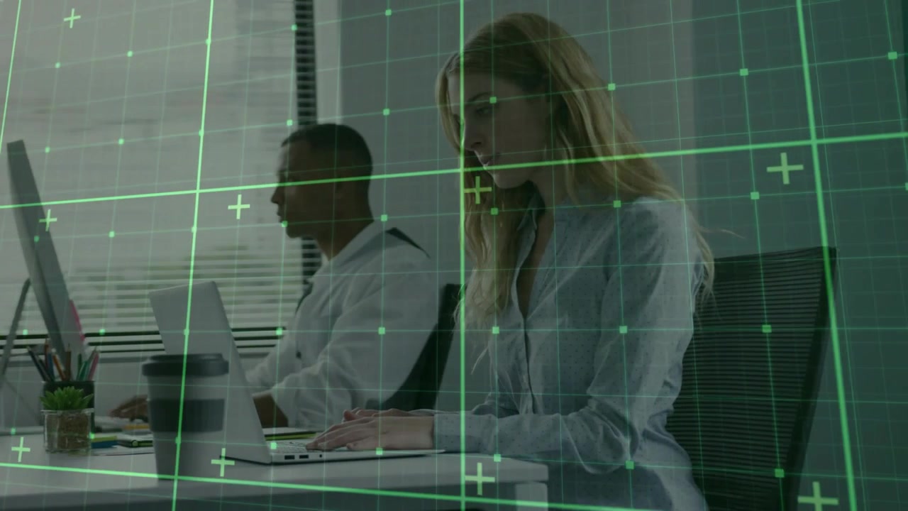 Kvinde taster på bærbar computer, mens et grønt gitter driver hen over kontoret, og en mand ser på skærmen og arbejder.