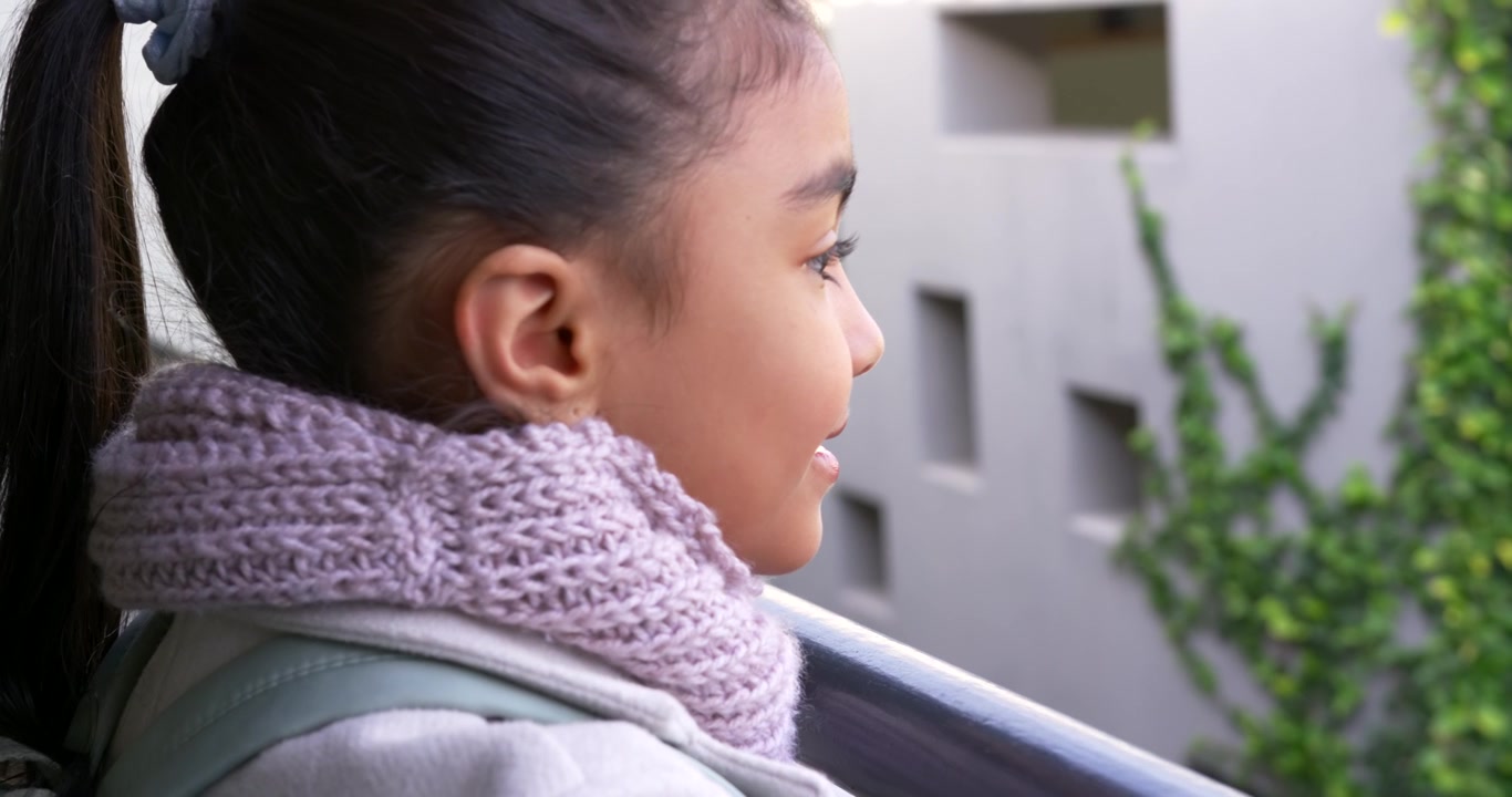 African American female youth hearing voice, turning and smiling on balcony and holding lilac scarf
