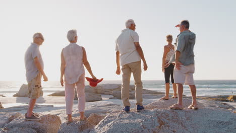 Rückansicht-Von-älteren-Freunden,-Die-Im-Sommergruppenurlaub-Auf-Felsen-Stehen-Und-Auf-Das-Meer-Blicken