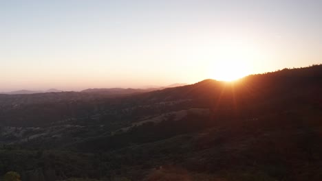 Amplia-Toma-Aérea-Del-Sol-Asomándose-Sobre-Una-Cresta-De-Montaña-Al-Atardecer