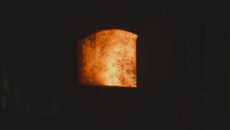 bright fire burns in open furnace chamber in dark workshop