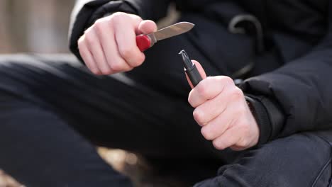 un hombre irreconocible afilando una navaja multiherramienta en un campamento al aire libre de cerca