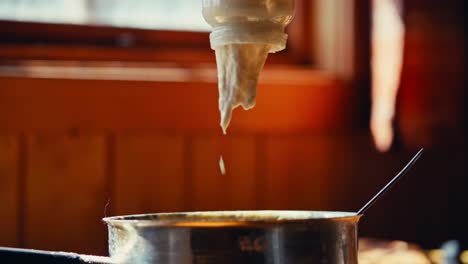 pouring thick white cream from a jar into a pan. close-up shot