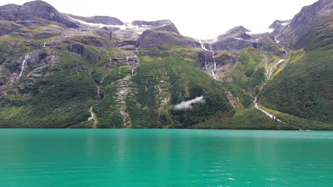 Aerial pullback of turquoise waters of Lake Lovatnet in Norway, surrounded by mountains and lush greenery