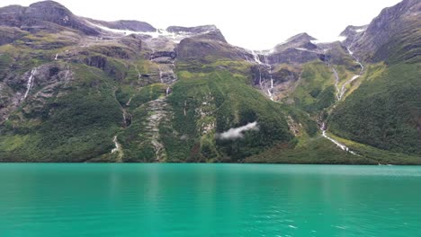 aerial pullback of turquoise waters of lake lovatnet in norway, surrounded by mountains and lush greenery