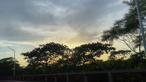 pov conduciendo a través de la carretera durante la puesta de sol amarilla dorada sobre los árboles en sylhet
