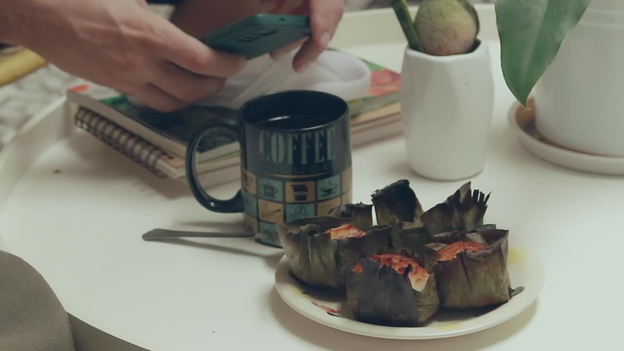 Fiddling with a smartphone while eating bingka or traditional Filipino rice cake and drinking coffee during an afternoon merienda