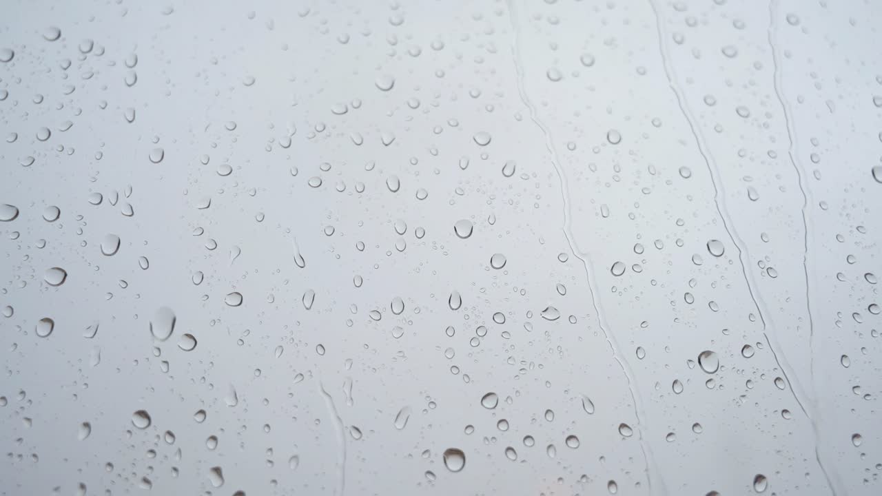 se ve a través de un vidrio de ventana una filmación cercana en cámara lenta de fuertes gotas de lluvia