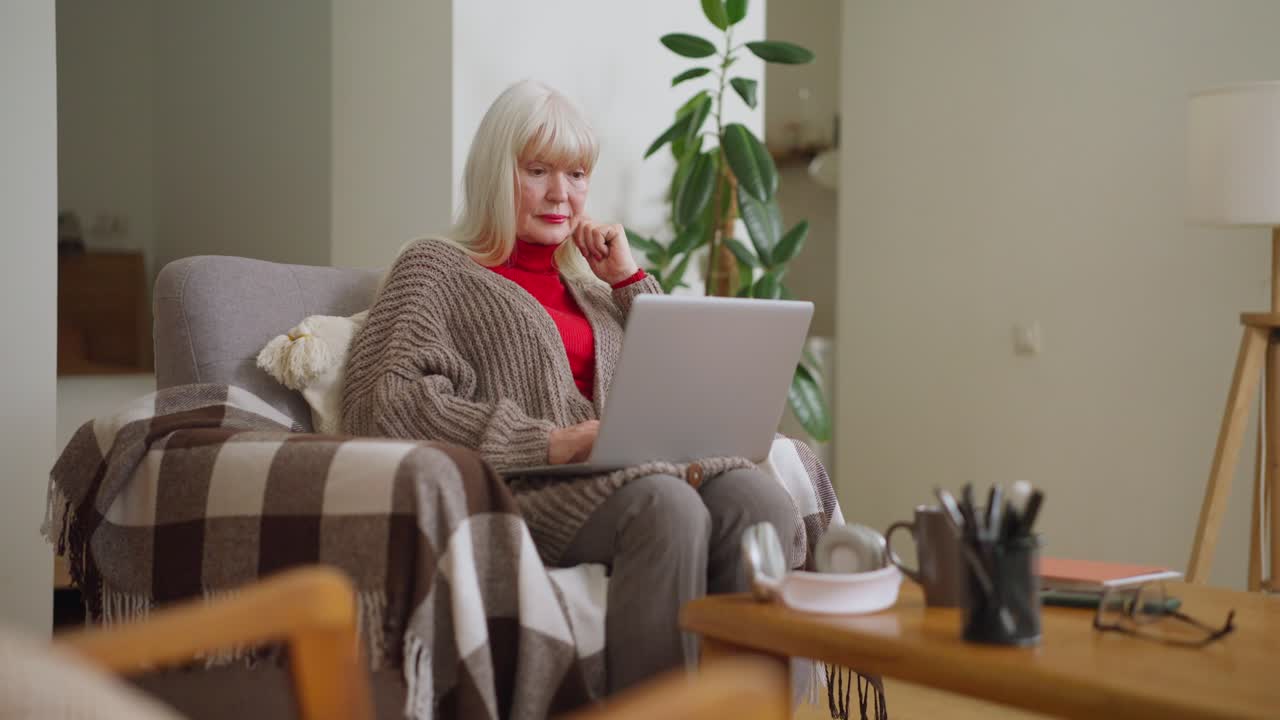 거실에서 노인 여성이 노트북을 사용하고 있습니다.