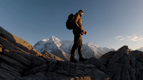 man hiking on a mountain summit with snow-capped peaks