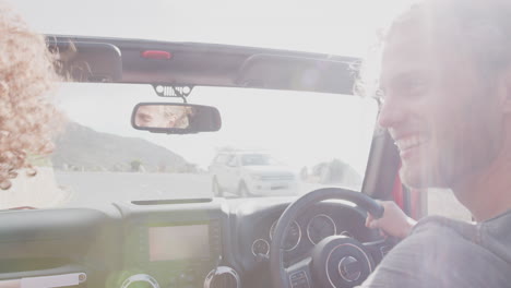 una pareja joven conduciendo un coche de alquiler abierto en las vacaciones de verano.