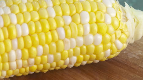 slow motion close up of a fresh, ripe corn on the cob rolling along a wood cutting board