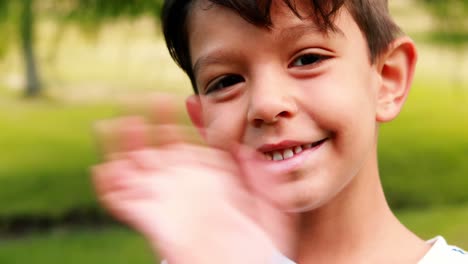 Lächelnder-Junge-Winkt-An-Einem-Sonnigen-Tag-Im-Park-Mit-Der-Hand