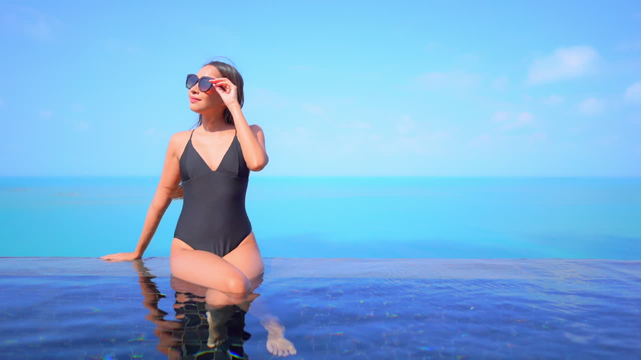 Schlanke exotische Frau im Badeanzug am Infinity-Pool mit endlos blauem tropischem Horizont im Hintergrund, Vollbild