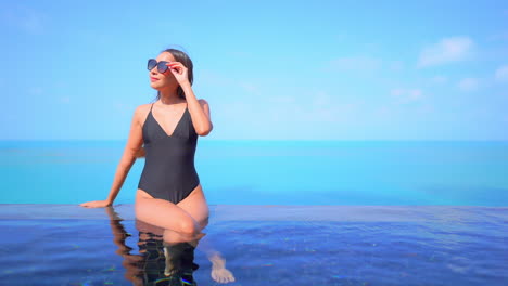 schlanke exotische frau im badeanzug am infinity-pool mit endlosem blauen tropischen horizont im hintergrund, vollformat