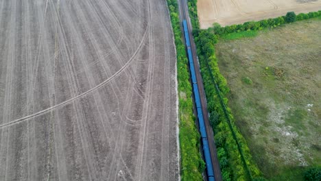 Disparo-De-Drones-De-Un-Tren-Azul-En-Un-Ferrocarril-Bordeado-De-árboles-Que-Atraviesa-El-Campo-Británico