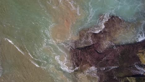 aerial top down view of ocean wave foaming and splashing from above rolling and breaking on empty ocean beach
