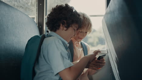 two pupils playing games on phone sitting school bus. boys using smartphone.